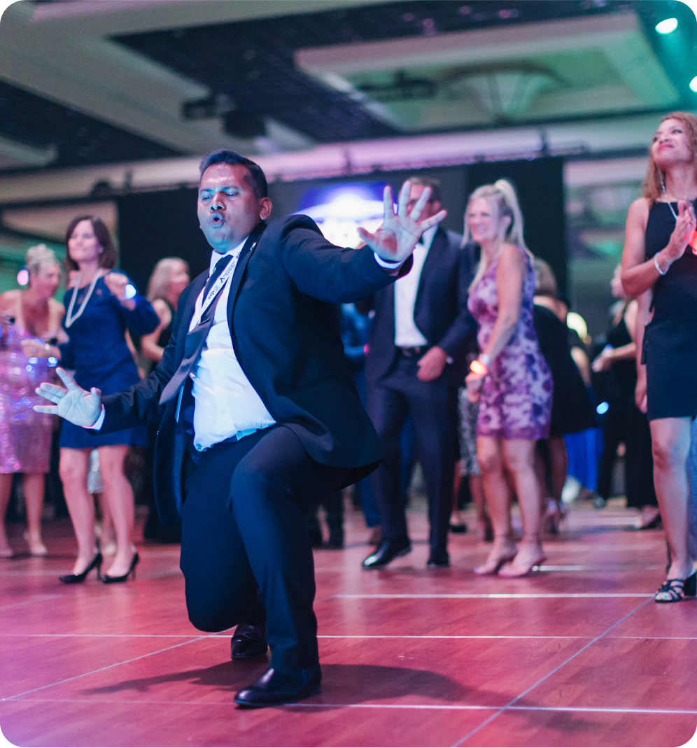 A man dancing at a formal event with others in the background.