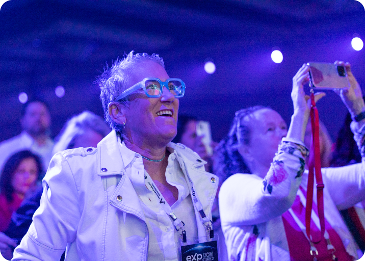 A man and a woman smiling during a conference session, with bright blue lighting.