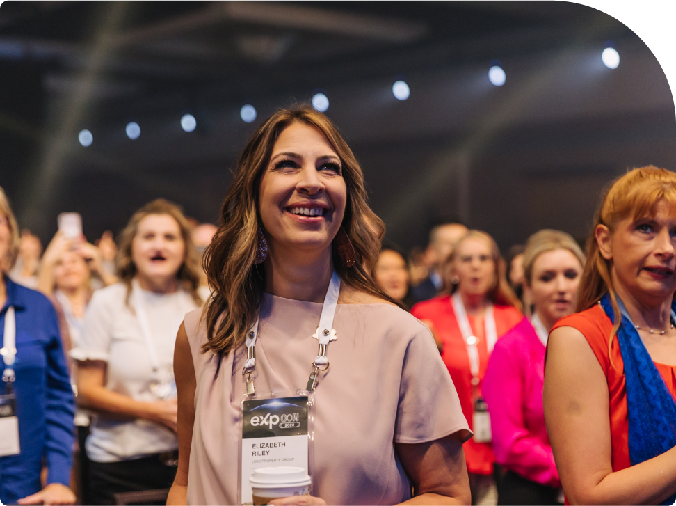 A woman smiling and standing in a crowd at a conference, wearing an eXp lanyard.