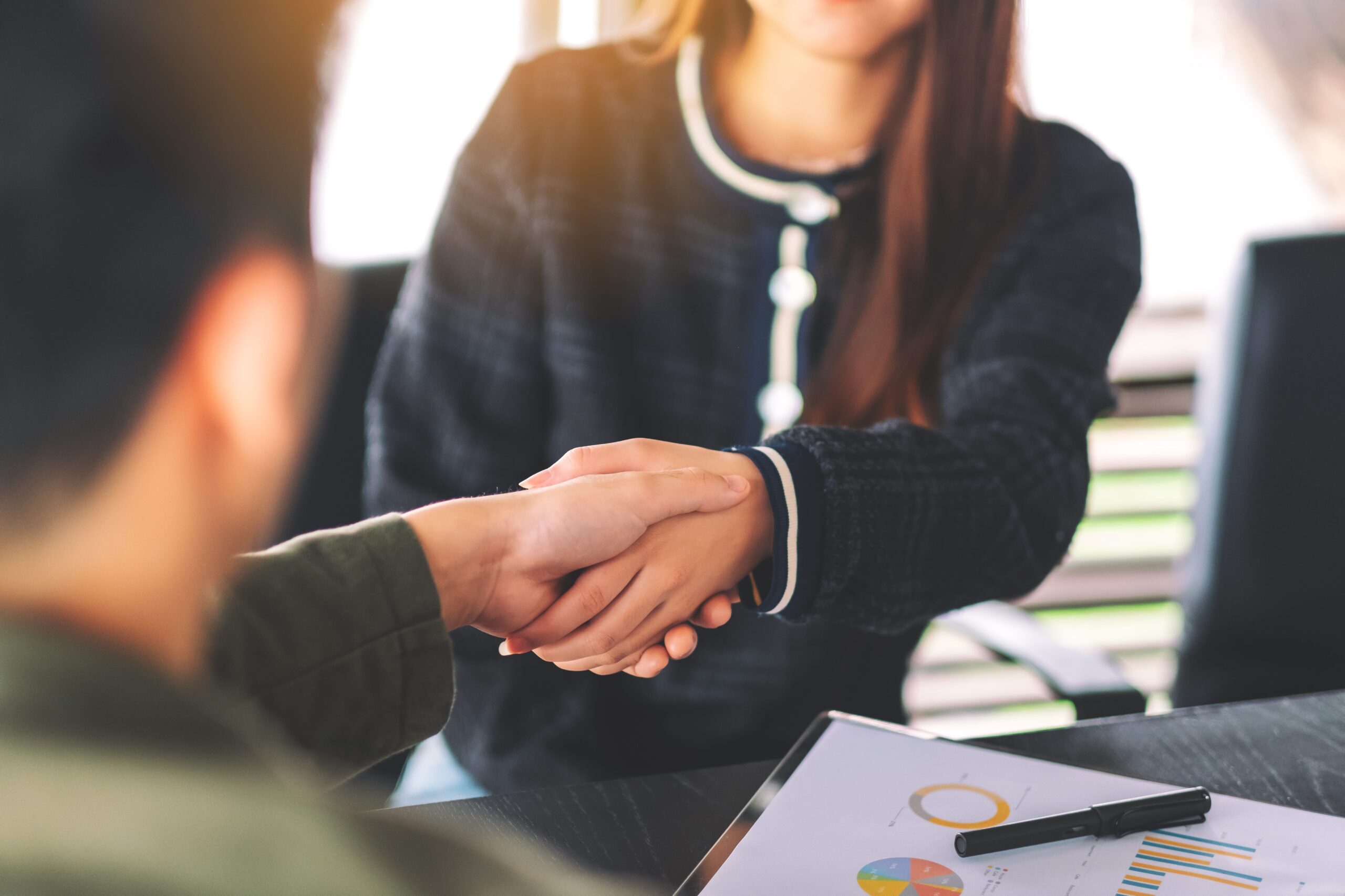 A handshake between two individuals, with a contract or document in front of them.