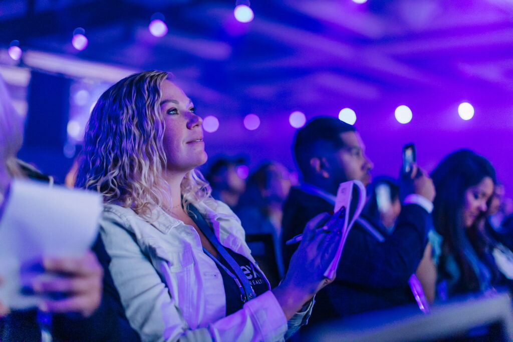 A woman watching the event attentively and holding a tablet, with blue and purple stage lighting in the background.