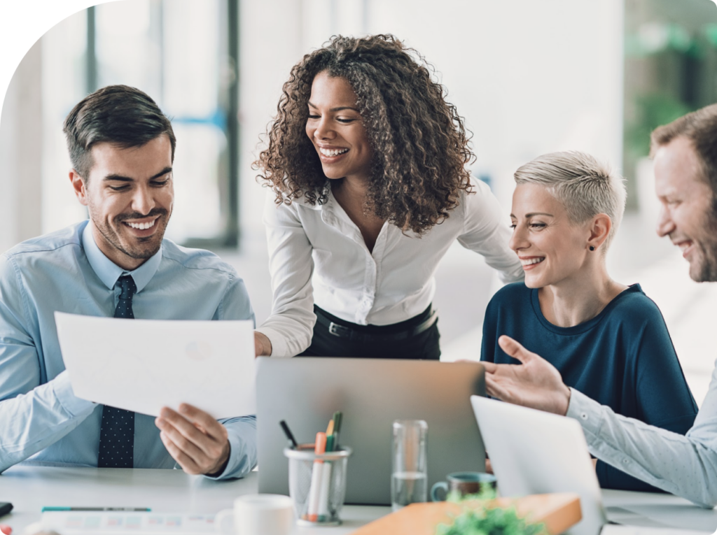 A group of business professionals smiles while reviewing a document together, showcasing teamwork and collaboration.